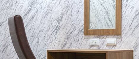 A corner desk with a chair, a mirror, and a marble wall.
