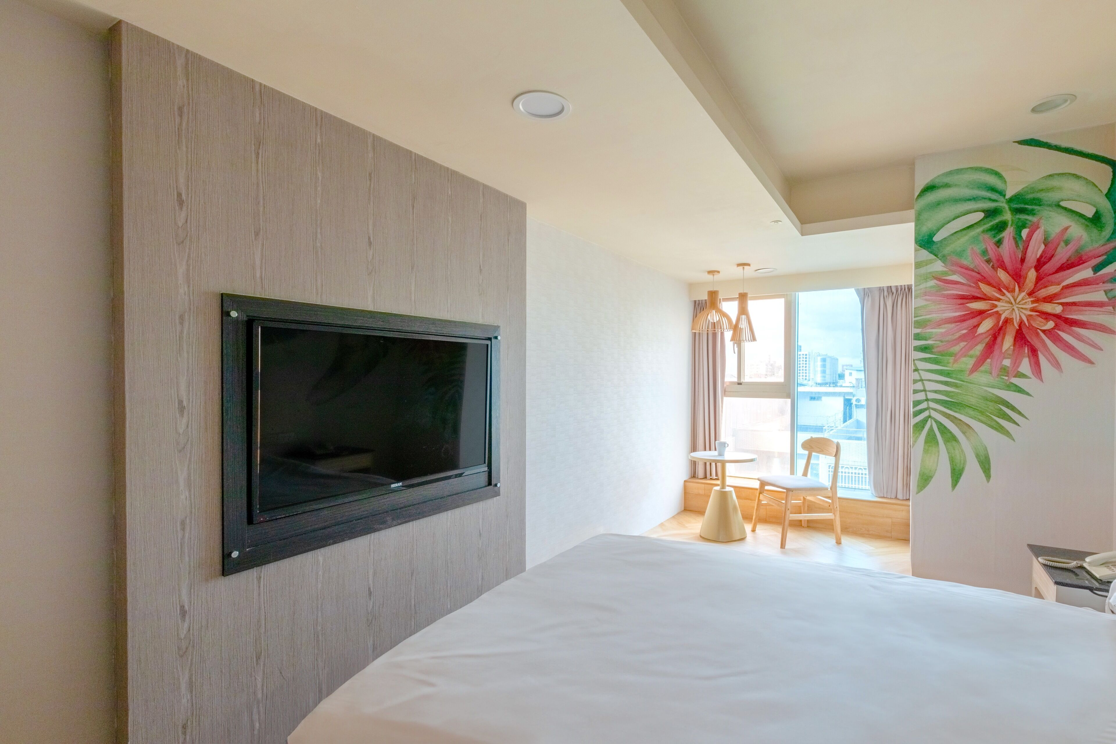 Ein Hotelzimmer mit einem großen Bett, einem Wand-Fernseher, einer Essecke mit Tisch und Stühlen sowie einem großen Fenster mit Blick auf die Stadt.