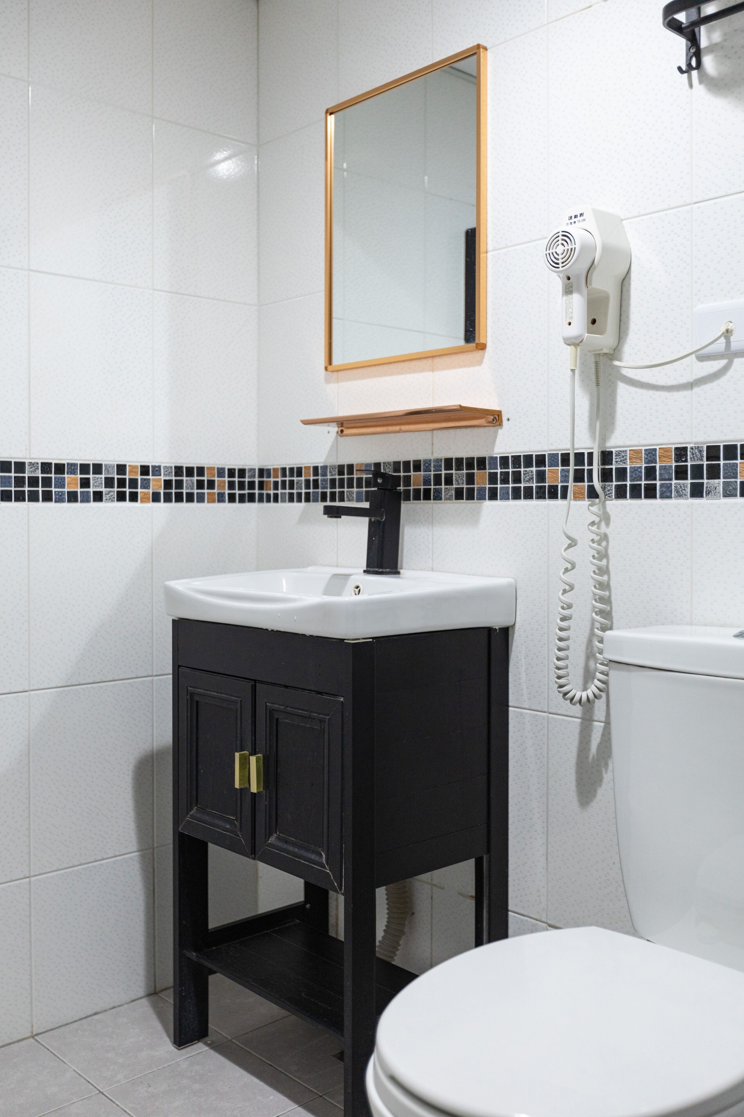 Un baño con un lavamanos blanco, un mueble negro y un espejo encima.