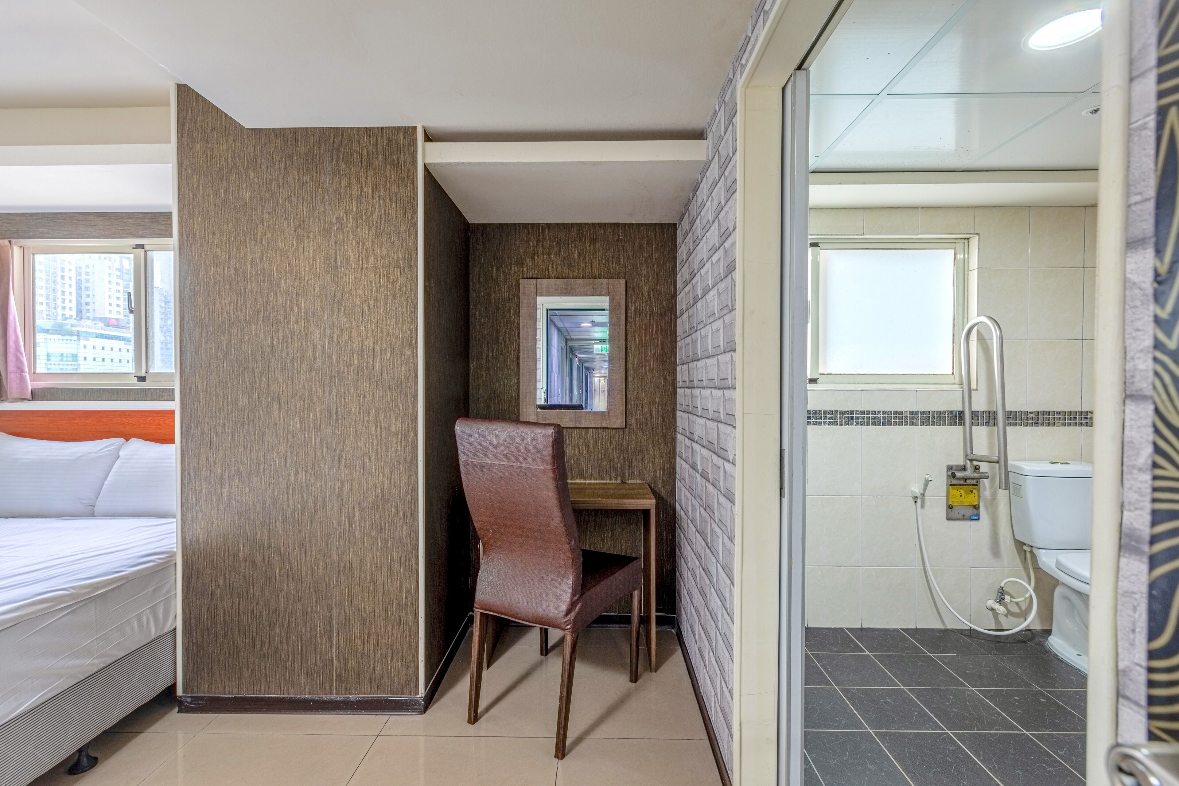 A hotel room with a bed, a desk, a chair, a shower, and a toilet.