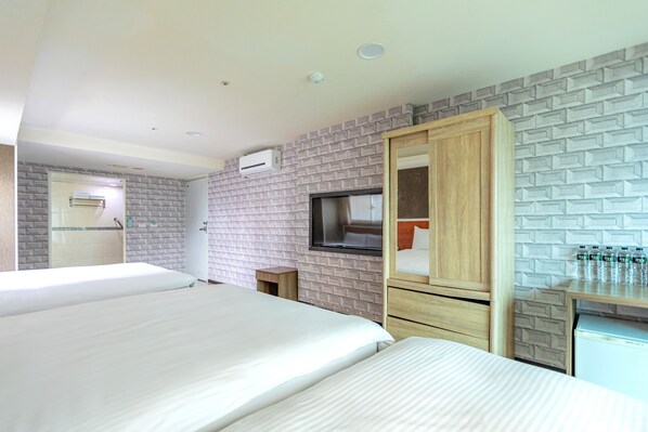 Quarto de hotel com duas camas, televisão, guarda-roupa e uma pequena cozinha.