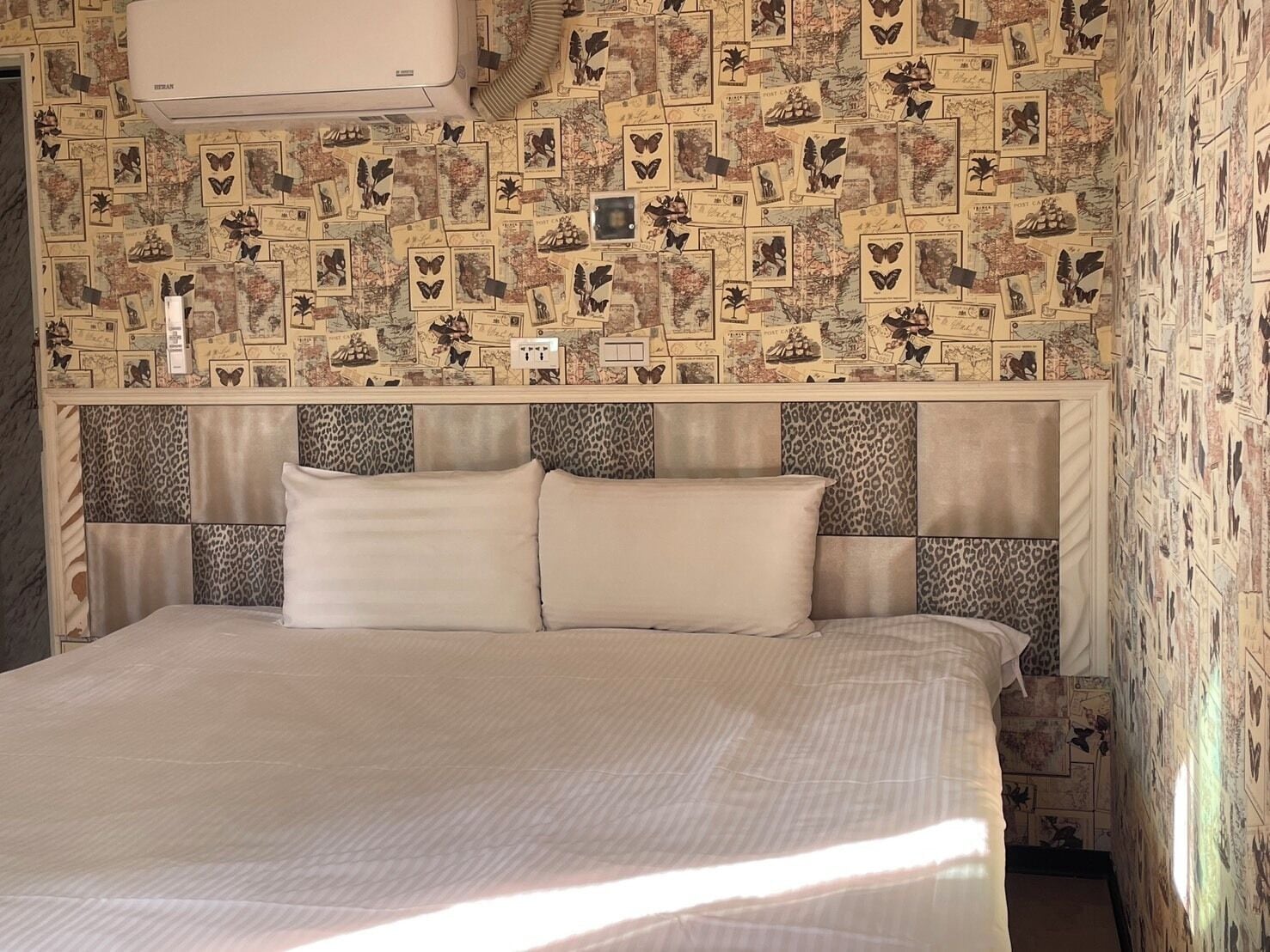 A hotel room with a bed, a headboard with a leopard print pattern, and a wall covered with postcards.