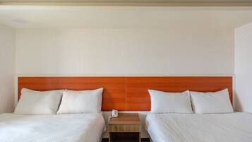 A hotel room with two beds, a wooden headboard, a bedside table with a phone, and a neutral-colored wall.