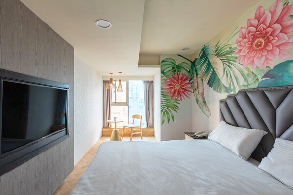 Une chambre d’hôtel dotée d’un grand lit, d’un téléviseur à écran plat fixé au mur, d’un plafond pourvu d’un éclairage encastré et d’une fresque murale aux motifs floraux éclatants.