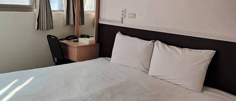 Quarto de hotel com uma cama grande, uma escrivaninha com cadeira, um espelho e uma janela com cortinas.