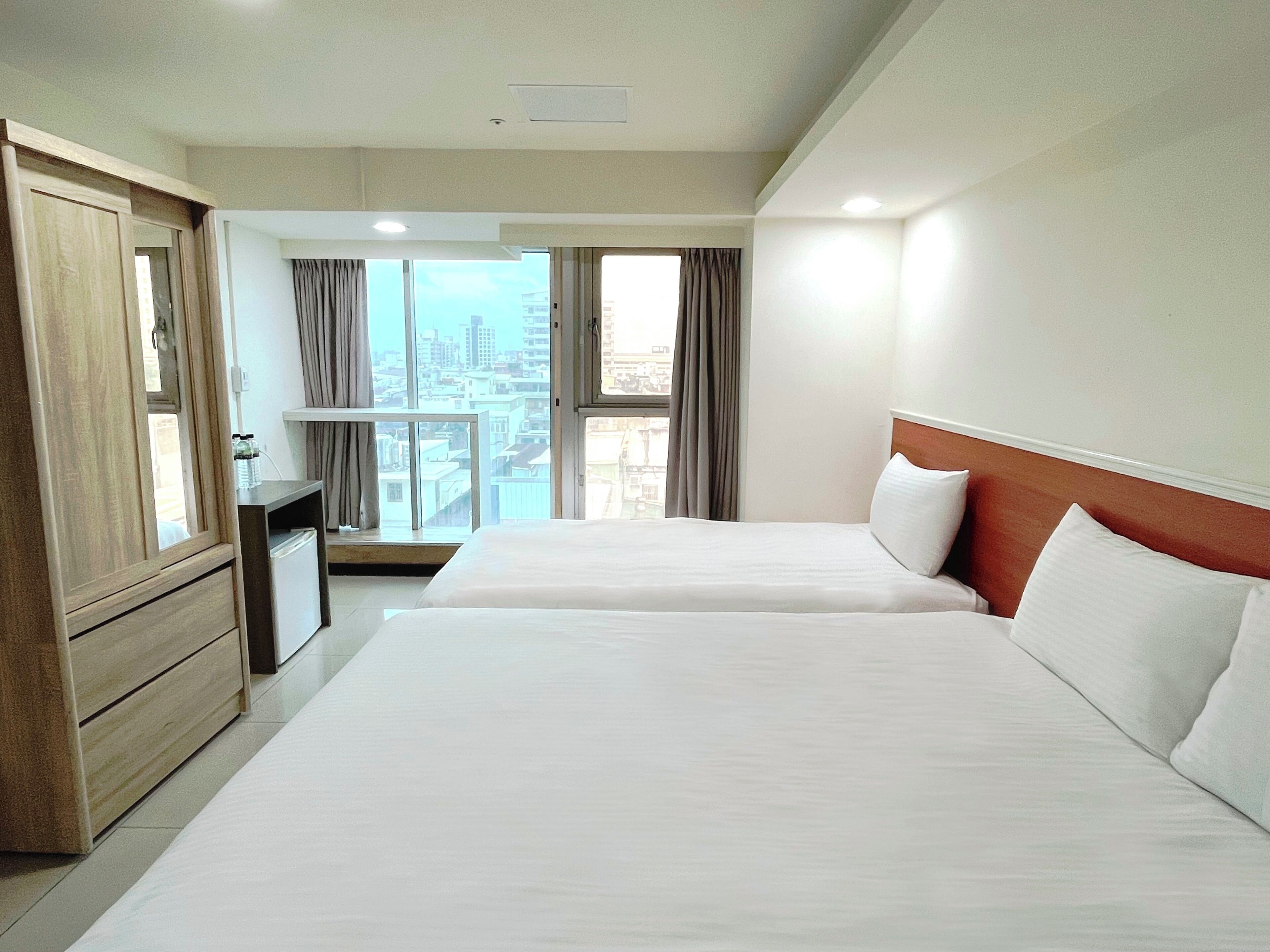 A hotel room with two beds, a desk, and a view of the city.