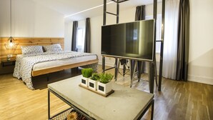 A modern bedroom with a bed, a TV on a stand, a small table with plants, and a window with curtains. - Atomic Apartment 02 (Belgrade)