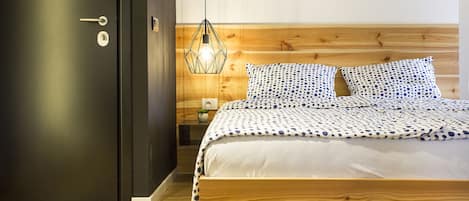 A bedroom with a wooden bed, a nightstand, a wall-mounted lamp, and a door with a keyhole.
