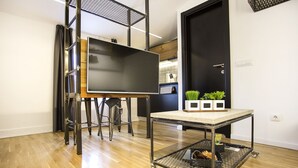 A modern kitchen with a large flat-screen TV, a dining table, and potted plants. - Atomic Apartment 02 (Belgrade)