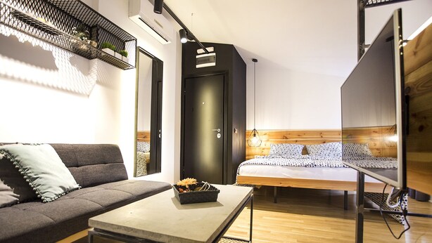 A modern room with a sofa, a bed, a small table, and a TV. - Atomic Apartment 02 (Belgrade)