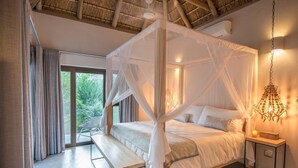 A bedroom with a four-poster bed, a bench, a bedside table, and a hanging light fixture.