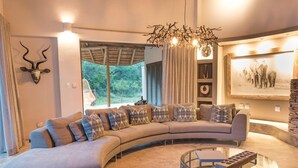 A modern living room with a curved sofa, a glass coffee table, and a chandelier.