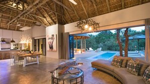 A spacious living area with a large round coffee table, a sofa with patterned cushions, and a dining area with a table and chairs.