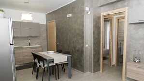 A modern kitchen with grey cabinets, a dining table with chairs, and a small refrigerator. - Casa Vacanze Fontana offered from 22/07/1929/07 / 19e from 08/25/19 to 31/08/19  (San Vito Lo Capo)