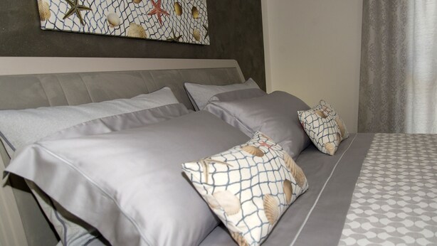 A neatly made bed with grey linens and patterned pillows, a grey headboard, and a wall-mounted artwork with a shell and starfish design. - Casa Vacanze Fontana offered from 22/07/1929/07 / 19e from 08/25/19 to 31/08/19  (San Vito Lo Capo)
