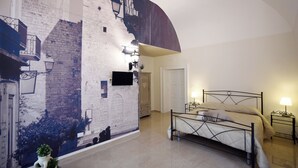 A bedroom with a bed, a nightstand, a wall-mounted TV, a door, and a wall mural. - Kapsott B&B (Bisceglie)