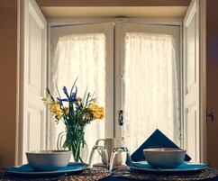 Un comedor con una mesa dispuesta para dos personas, un florero y una jarra.
