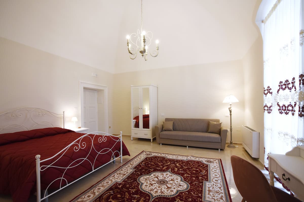 Un dormitorio con cama, sofá, espejo y candelabro.