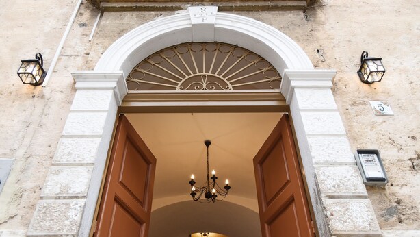 An arched entrance with a chandelier, two wall-mounted lanterns, and a stone wall. - Kapsott B&B (Bisceglie)