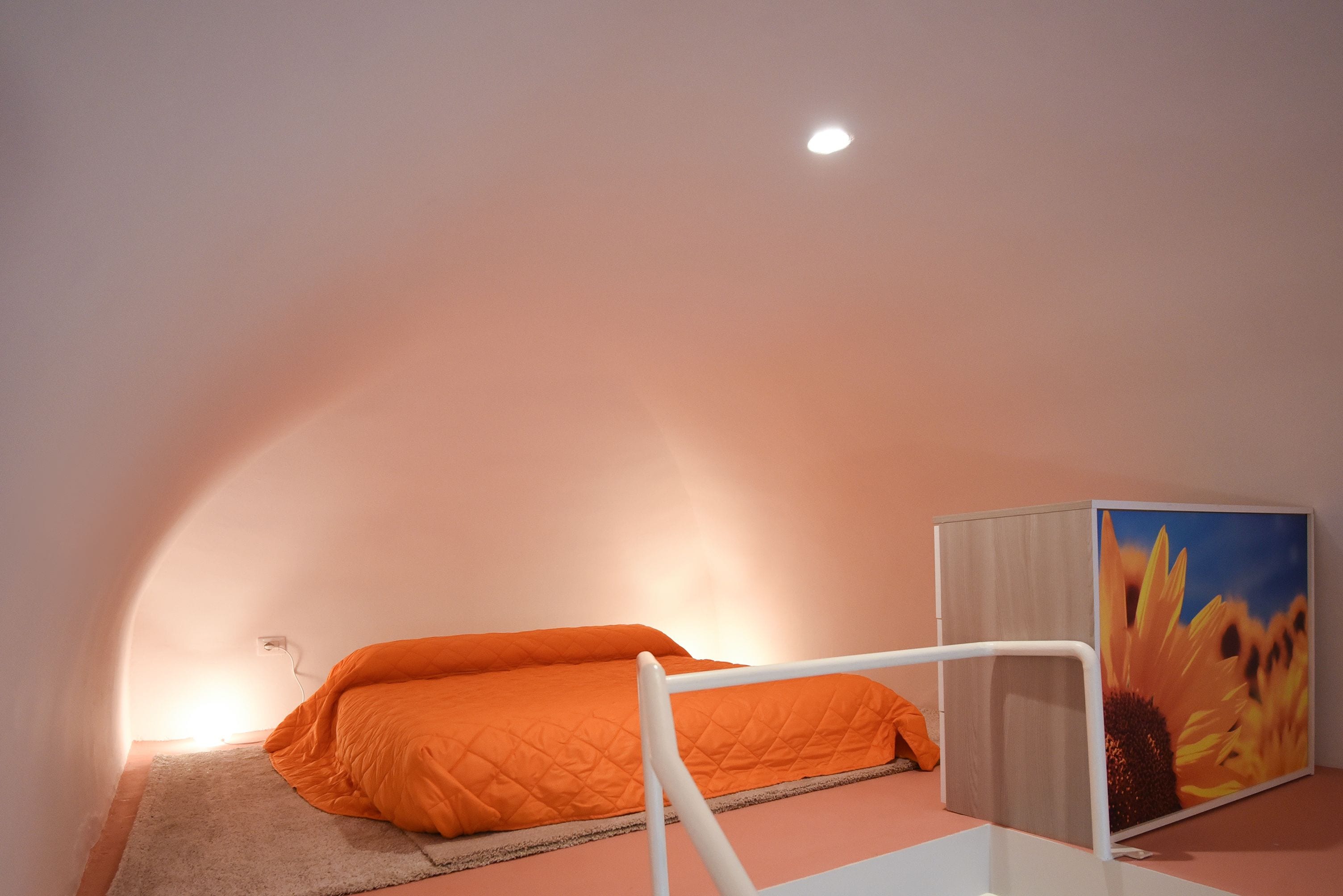 A bedroom with a single bed, a white bedside table, a nightstand, and a large window.