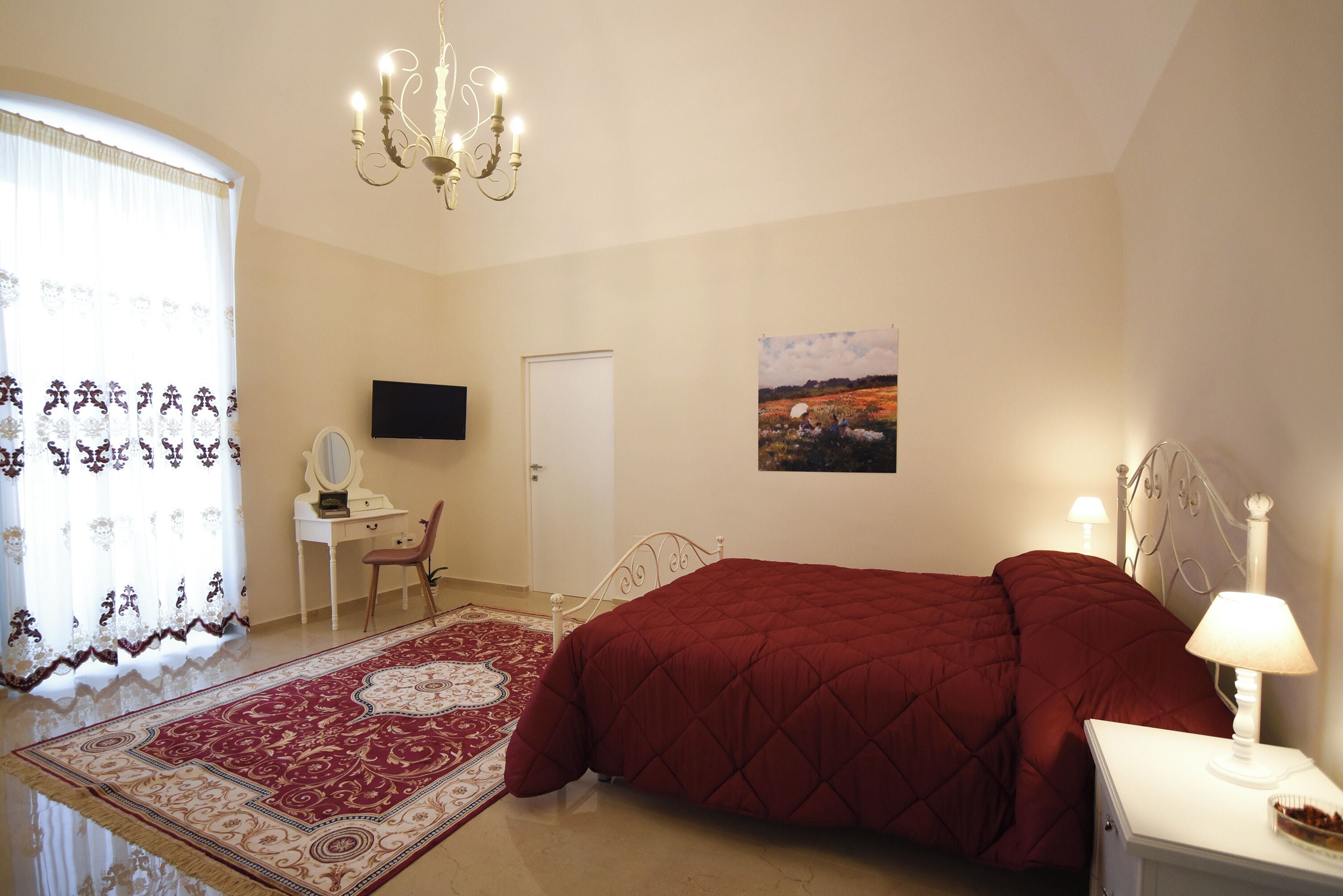 A bedroom with a bed, a desk, a chair, a television, a door, and a painting on the wall.