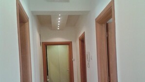 Een gang met houten vloer, witte wanden en een plafond met inbouwverlichting.