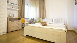 Een slaapkamer met een bed, een kaptafel, een stoel, een tafeltje en een raam met gordijnen.