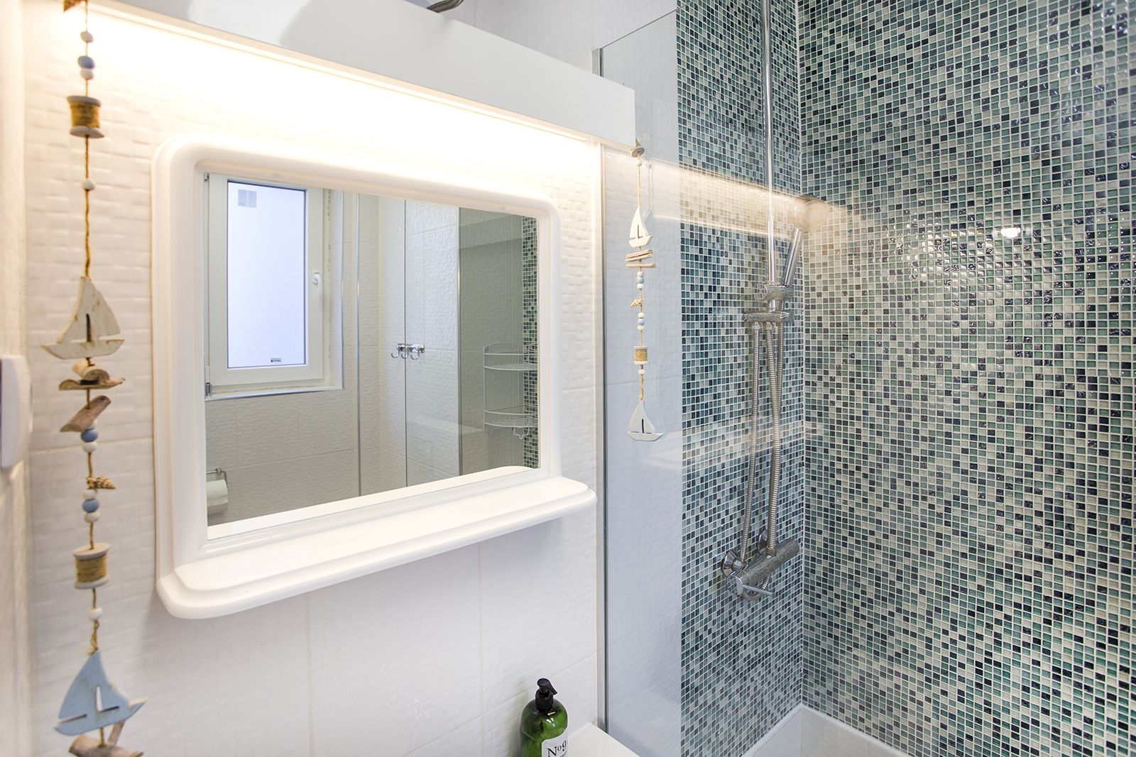 A bathroom with a white vanity, a mirror, a shower with mosaic tiles, and a hanging ornament.