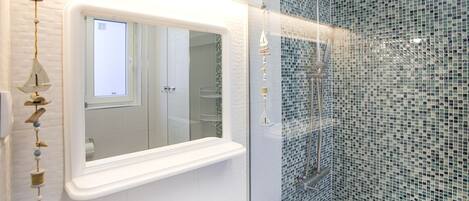 A bathroom with a white vanity, a mirror, a shower with mosaic tiles, and a hanging ornament.