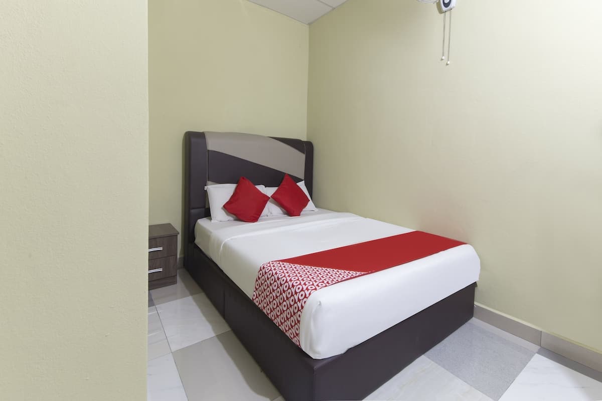 A neatly made bed with a white and red bedspread, a dark headboard, and two red pillows. There is a small bedside table with a lamp, and a ceiling fan above the bed.