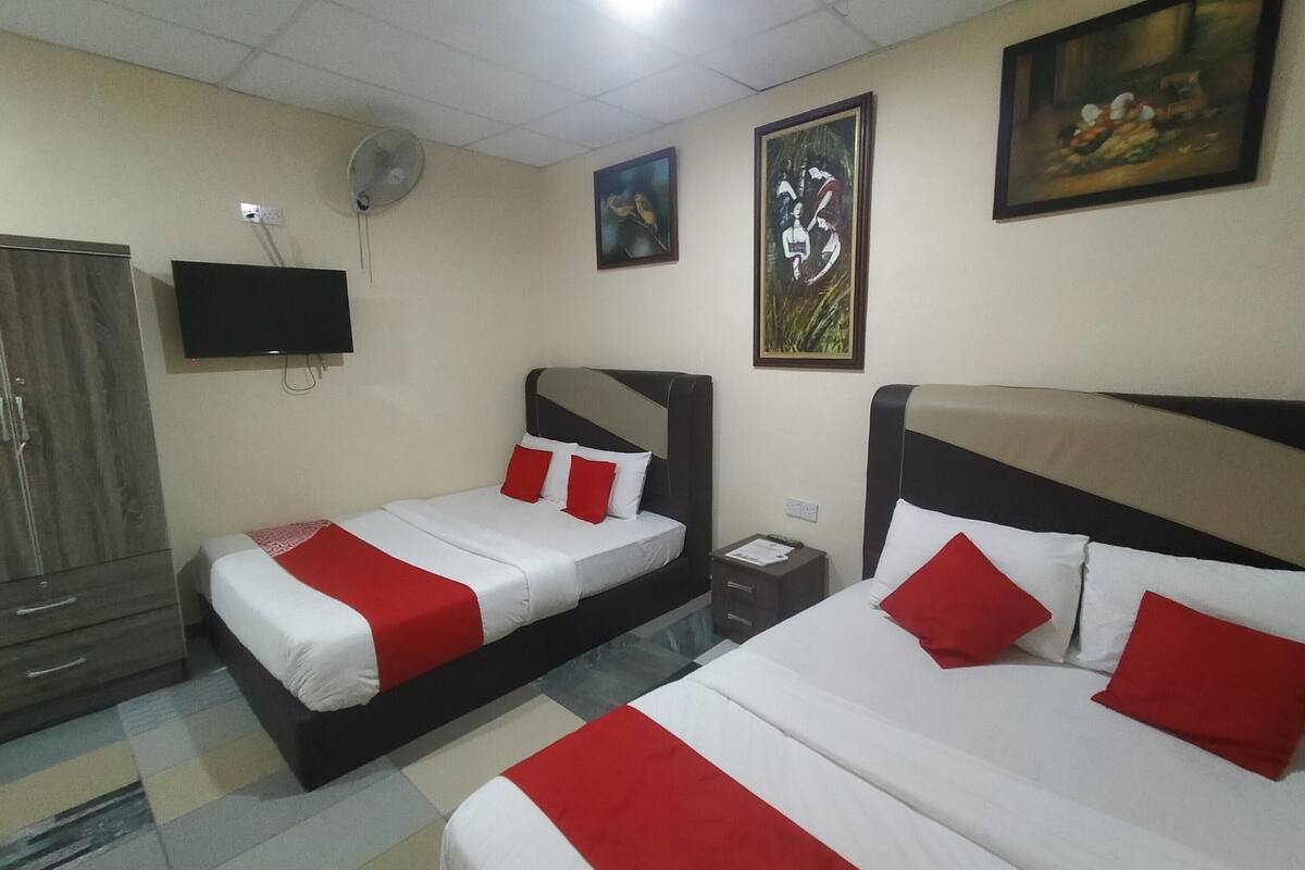 A hotel room with two beds, each with red and white bedding, a flat-screen TV mounted on the wall, and artwork above the beds.