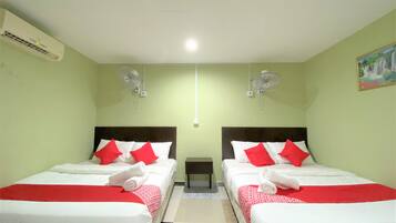 A hotel room with two beds, each with red and white bedding, a small table, and two wall-mounted fans.