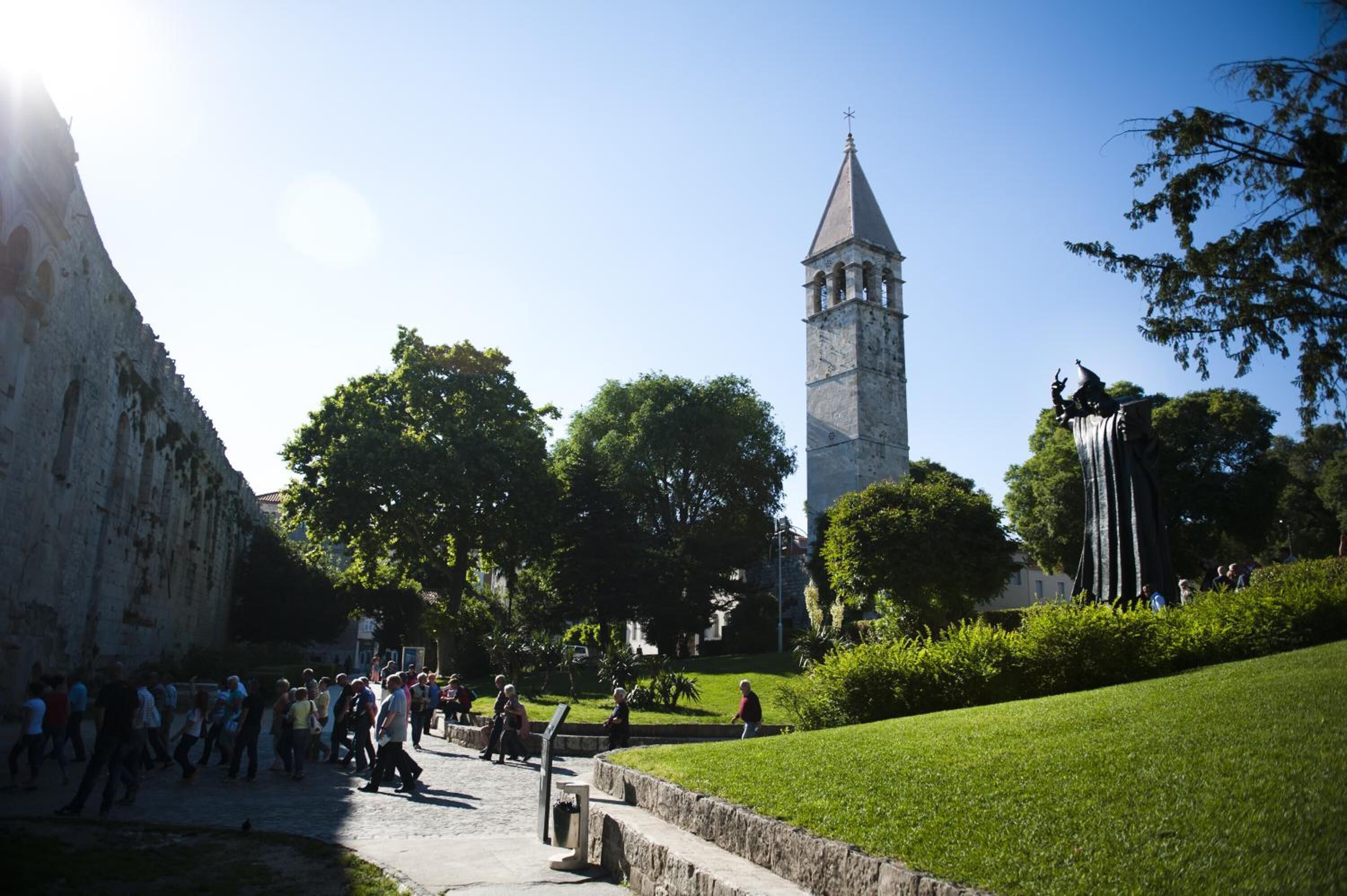 A historic building with a tall tower, a statue, and a well-maintained lawn.
