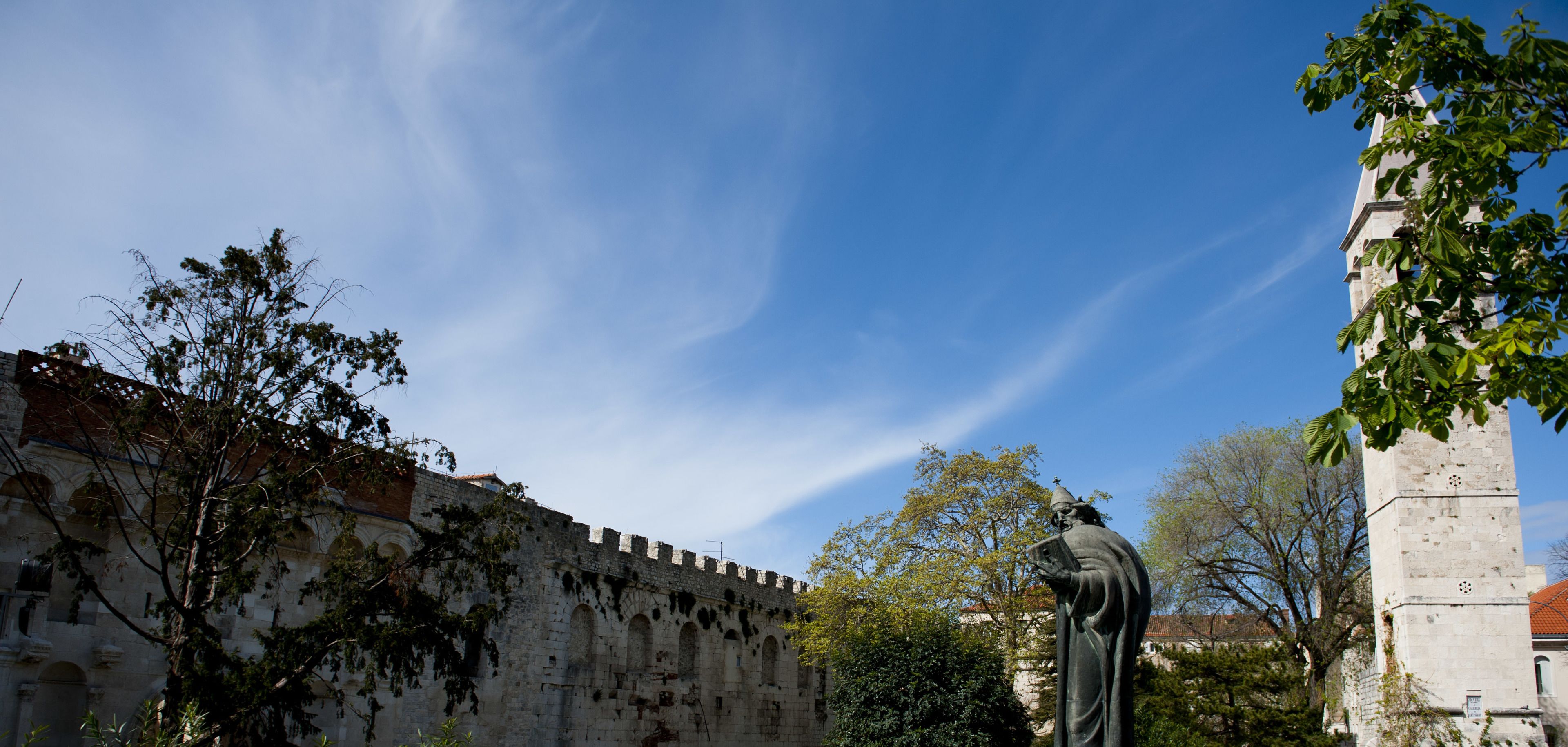A historic stone wall with arched windows and a statue in front.