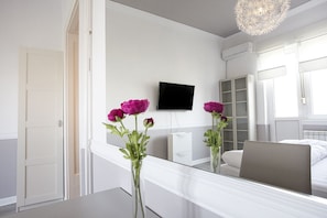 A hotel room with a bed, a TV mounted on the wall, a mirror, and a vase with flowers on the bedside table. - Apartment Harizma (Belgrade)