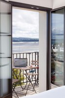 Un balcón con una computadora portátil sobre una mesa, una silla y vistas a la playa y edificios.