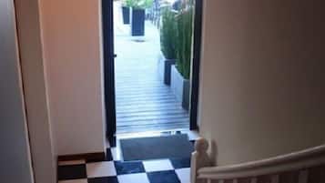 Una escalera con piso a cuadros blanco y negro que lleva a un espacio exterior con plantas y una parrilla.