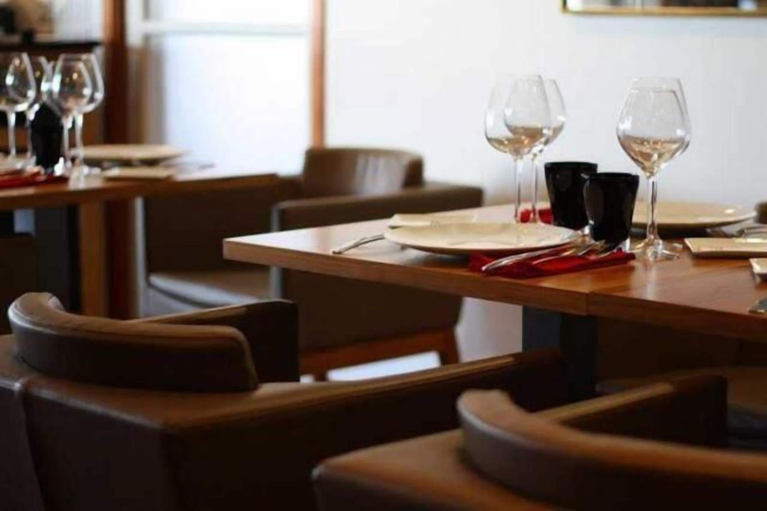 A restaurant setting with tables set for dining, each with a wine glass and cutlery.