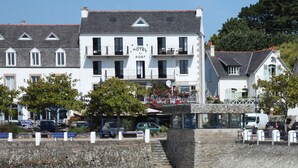 Et hotel med en hvid facade, flere balkoner og en stentrappe, der fører op til indgangen.