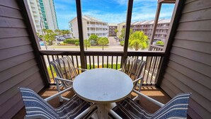 Een balkon met een ronde tafel en gestreepte stoelen, met uitzicht op een parkeerplaats en gebouwen.