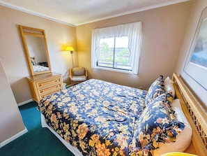 A bedroom with a bed, a dresser, a chair, a window with curtains, and a lamp.