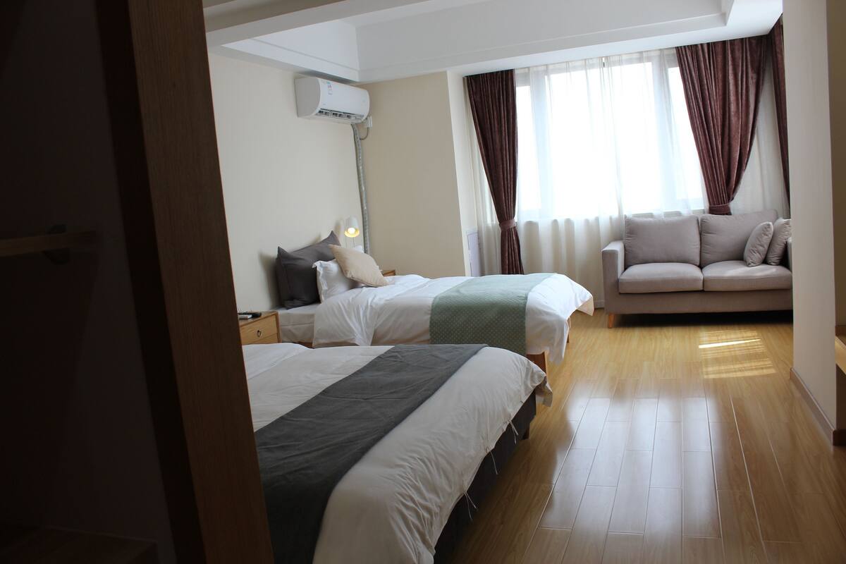 Une chambre d’hôtel avec deux lits, un canapé, une lampe et une fenêtre avec des rideaux.