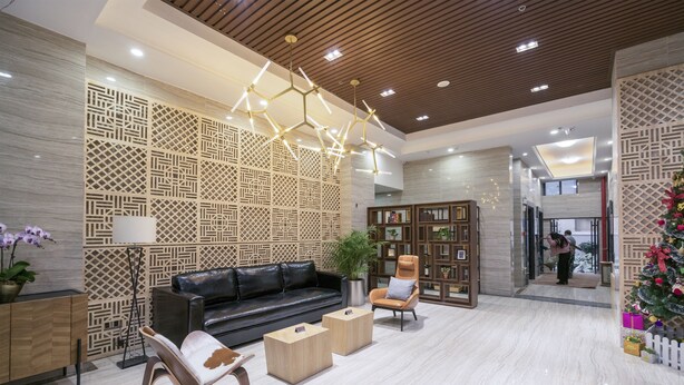 Een moderne lobby met een zwarte leren bank, houten salontafels en een decoratieve wand met geometrische patronen.