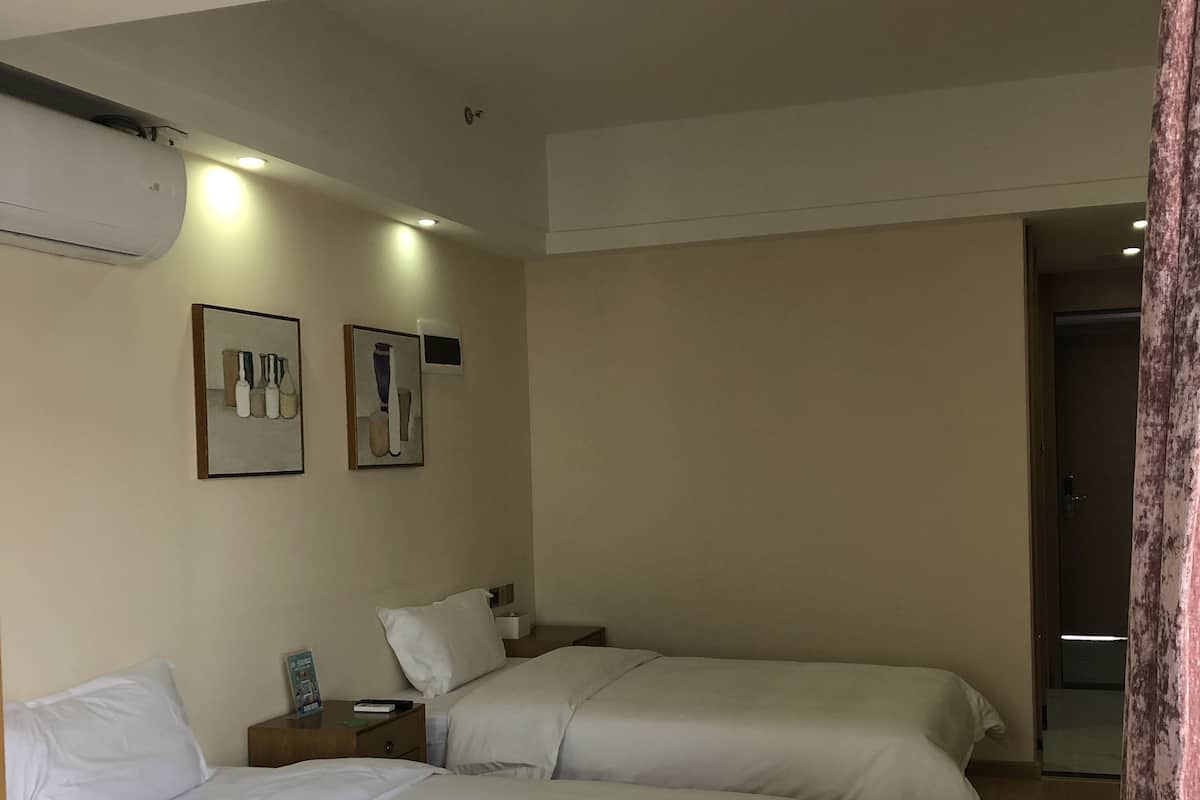 Une chambre d’hôtel avec deux lits, un plancher en bois et un climatiseur fixé au mur.