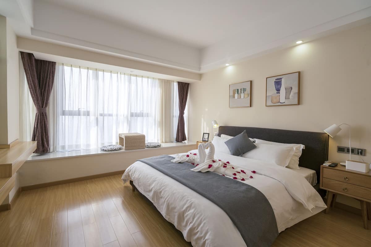 Une chambre d’hôtel avec un grand lit, une table de chevet, une commode, une fenêtre avec des rideaux et des œuvres d’art accrochées au mur.