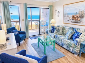 A room with a view of the ocean, a sofa with a tropical print, a glass coffee table, and a chair.