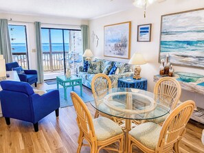 Ein Wohnzimmer mit Glastisch, Korbstühlen, einem blauen Sofa und Blick auf den Ozean.