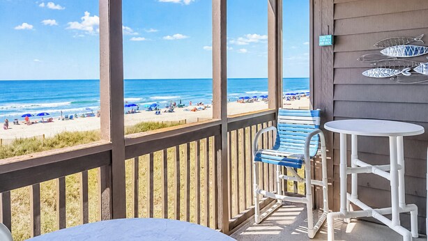 A balcony with a view of the beach, a blue chair, a white table, and a sign with fish decorations. - Experience Tilghman Beach and Racquet Club Unit 207! Oceanfront, Pools, Tennis, Close to Main Street! (North Myrtle Beach)