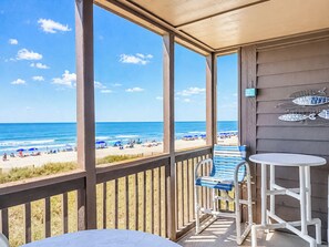 Un balcon avec vue sur la plage, une chaise bleue, une table blanche et un panneau décoré de motifs de poissons.
