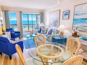 A room with a balcony, a sofa, a dining table, and chairs.